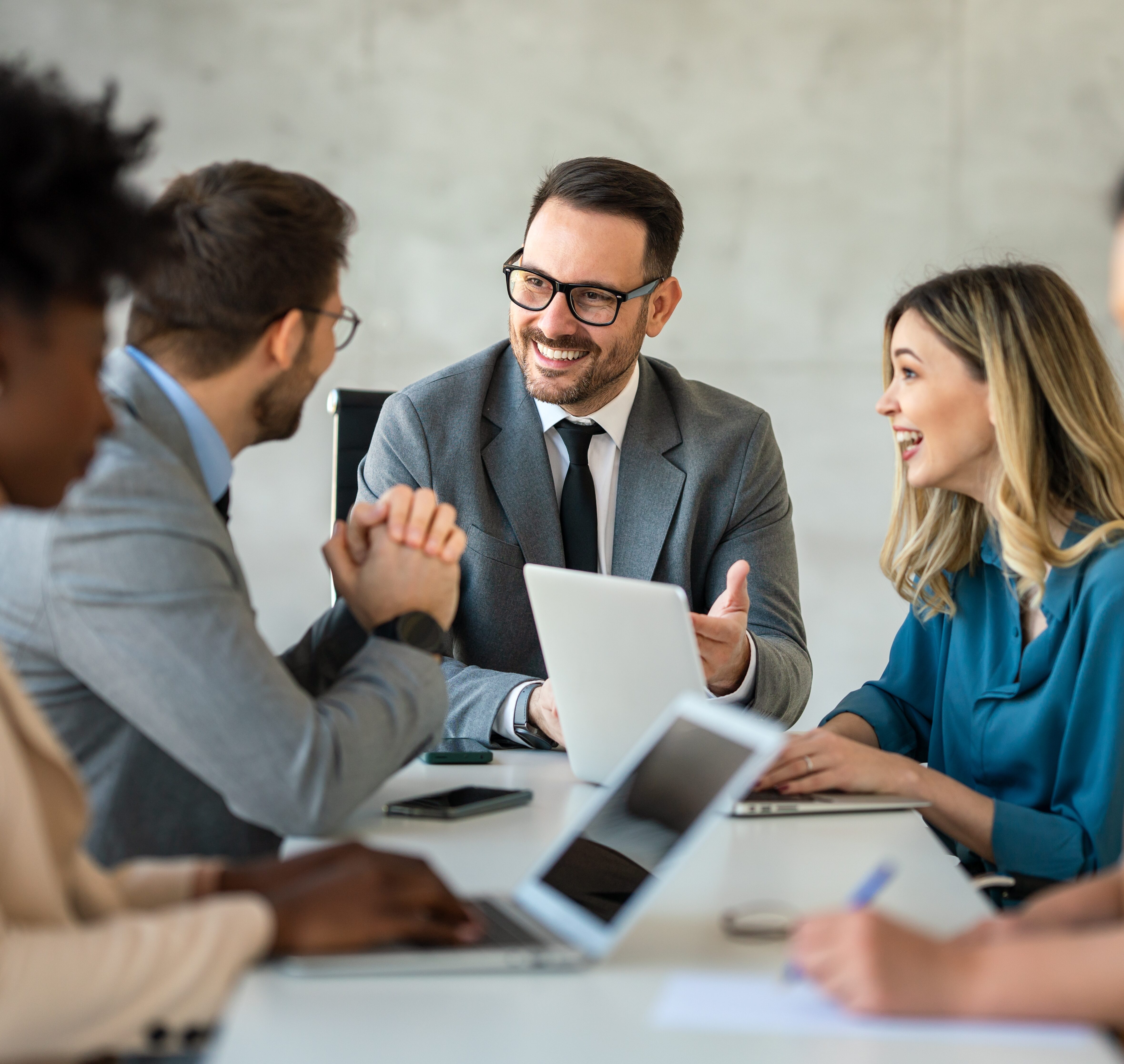 Four people in business attire sit at a conference table with laptops, engaged in a meeting and conversation about Providence Risk Insurance Services, as one man smiles and gestures.